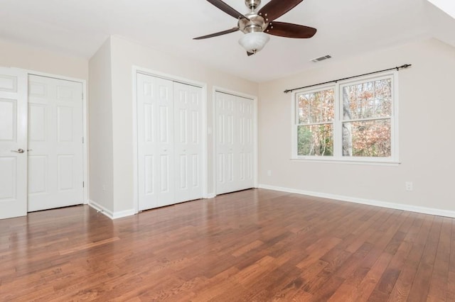 unfurnished bedroom with ceiling fan, two closets, and hardwood / wood-style flooring