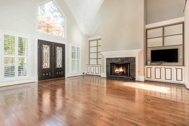 unfurnished living room with a tile fireplace, hardwood / wood-style floors, high vaulted ceiling, and french doors