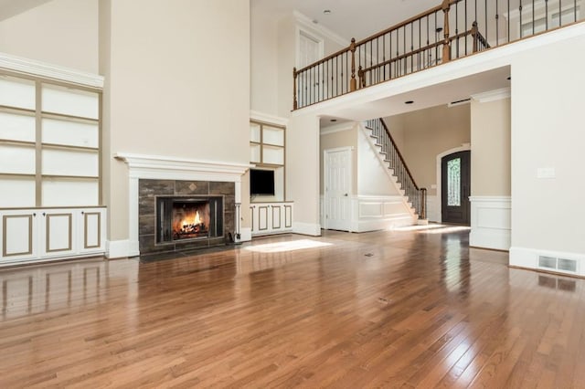 unfurnished living room with hardwood / wood-style floors, crown molding, a fireplace, and a high ceiling