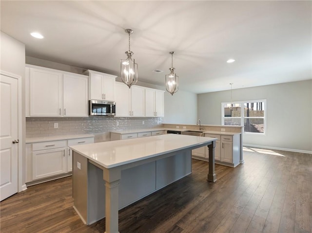 632 Eagles Nest Cir, Auburn, GA 30011 - kitchen featuring stainless steel microwave, a sink, decorative backsplash, a peninsula, and hanging light fixtures