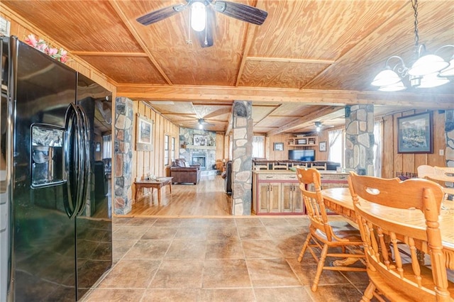 dining area featuring ceiling fan, a stone fireplace, wood ceiling, wood-type flooring, and wooden walls