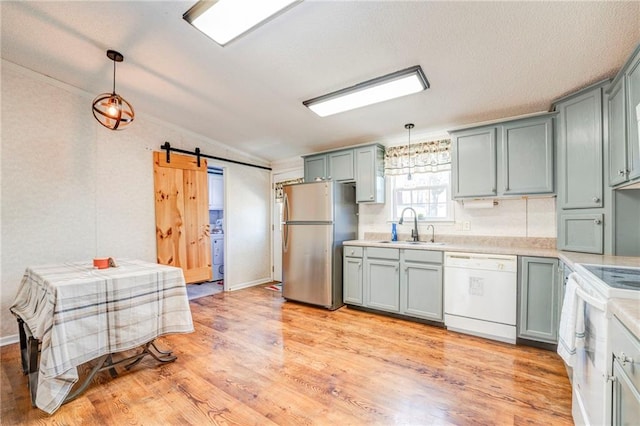 kitchen featuring light wood-type flooring, white appliances, pendant lighting, a barn door, and sink