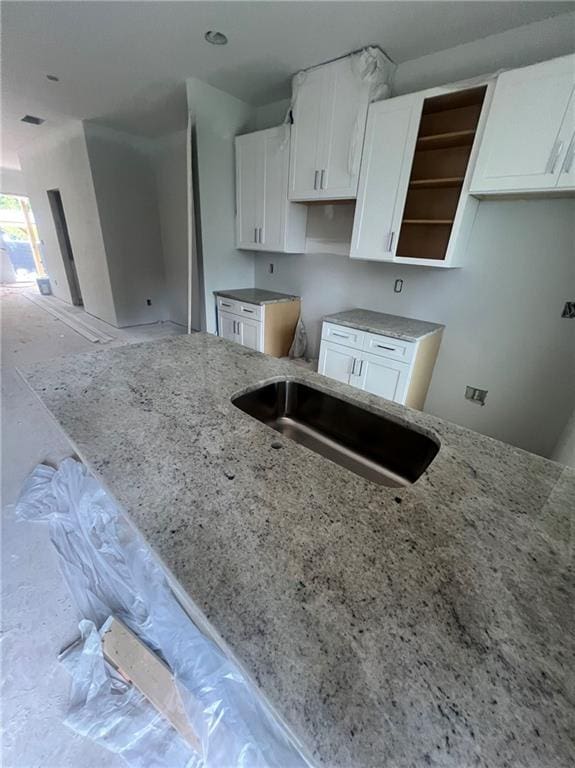 kitchen with white cabinetry, light stone counters, and sink