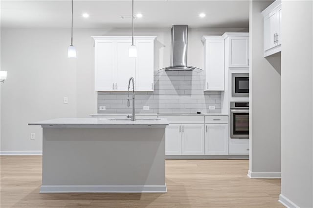 kitchen with an island with sink, white cabinets, decorative light fixtures, oven, and wall chimney exhaust hood