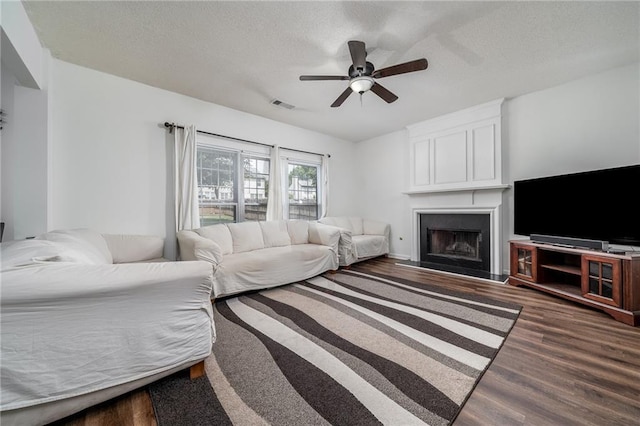 living room with visible vents, ceiling fan, dark wood finished floors, a fireplace, and a textured ceiling