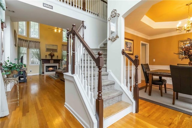 3780 Summit Gate Dr, Suwanee, GA 30024 - stairs with a warm lit fireplace, crown molding, wood finished floors, a chandelier, and ceiling fan