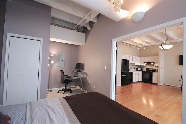 bedroom with black refrigerator, electric panel, light hardwood / wood-style flooring, and beamed ceiling