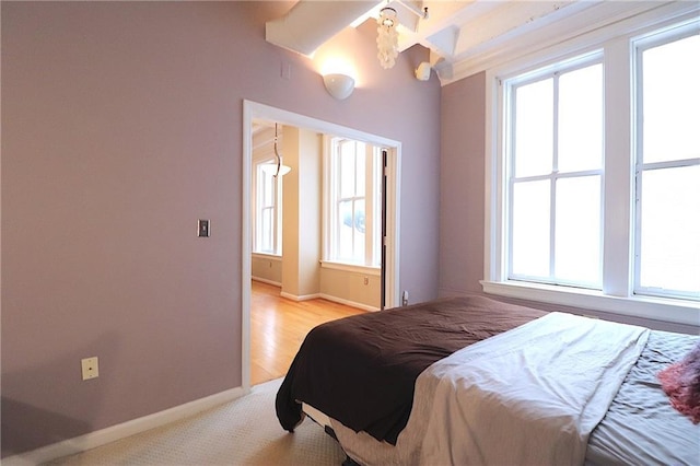 bedroom with multiple windows, beam ceiling, and light hardwood / wood-style floors