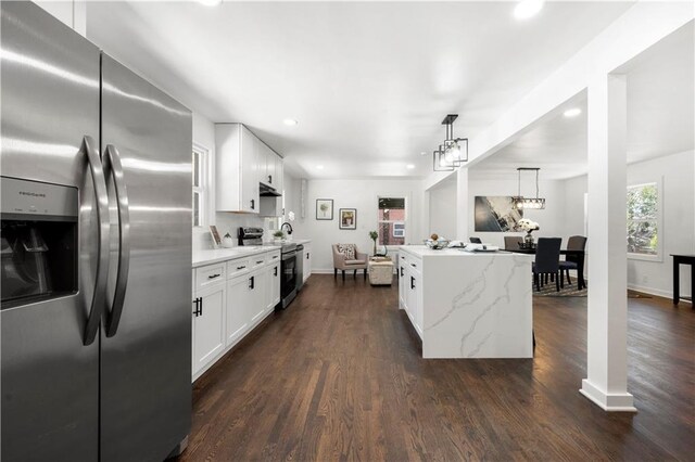 kitchen with light stone counters, decorative light fixtures, dark hardwood / wood-style floors, stainless steel appliances, and white cabinets