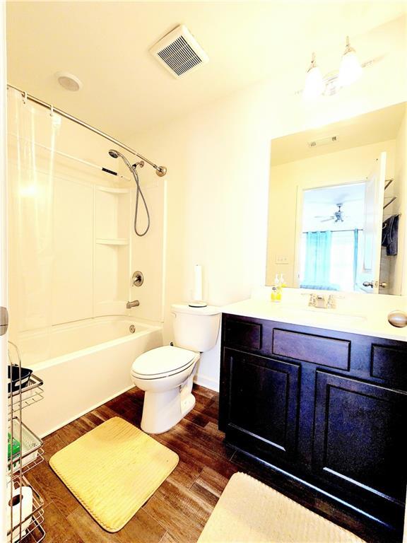 bathroom with visible vents, shower / washtub combination, toilet, wood finished floors, and vanity