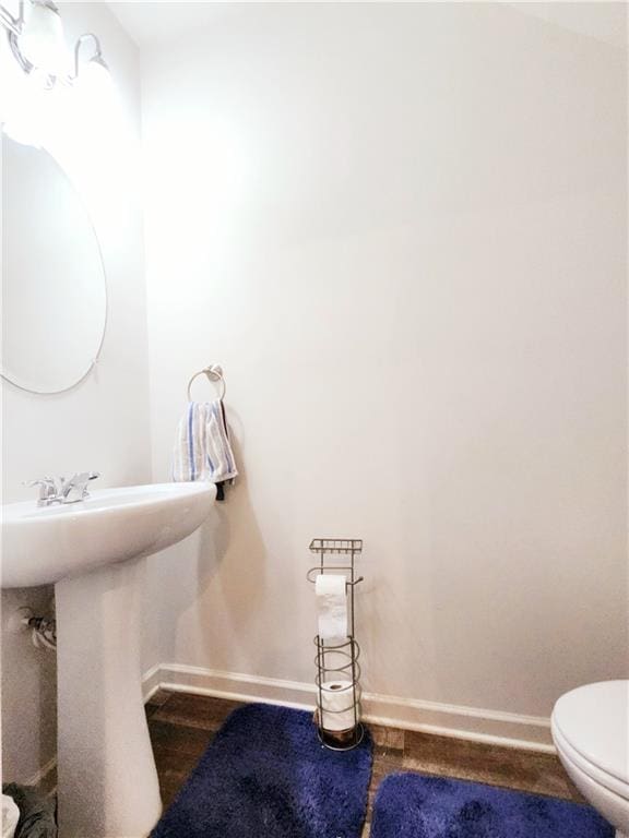 bathroom featuring wood finished floors, toilet, baseboards, and a sink