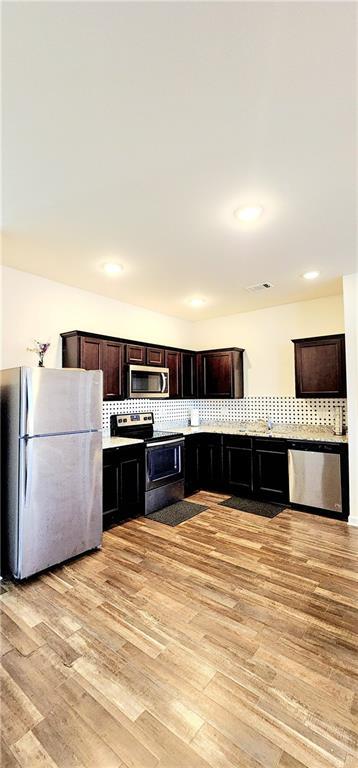 kitchen with visible vents, light wood-style flooring, tasteful backsplash, stainless steel appliances, and dark brown cabinetry