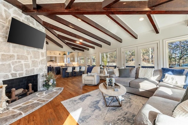 living room with hardwood / wood-style flooring, a stone fireplace, vaulted ceiling with beams, and french doors