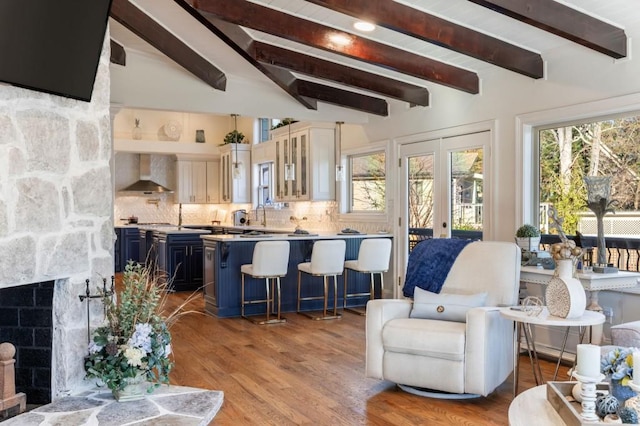 living room with french doors, a stone fireplace, sink, beamed ceiling, and light hardwood / wood-style floors