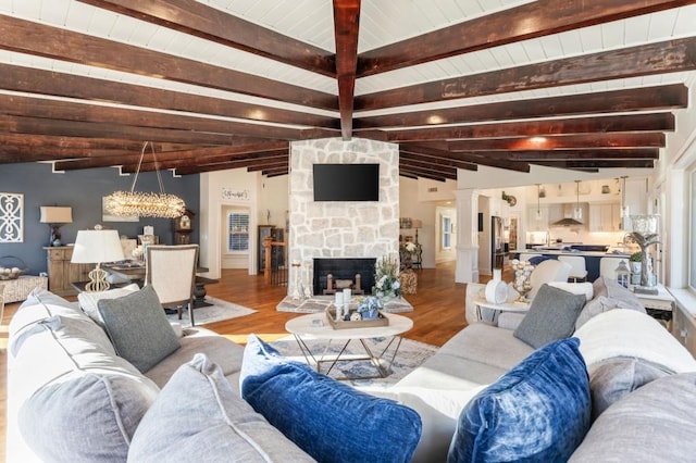 living room featuring a stone fireplace, lofted ceiling with beams, ornate columns, and light wood-type flooring