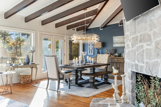 dining area featuring a stone fireplace, vaulted ceiling with beams, an inviting chandelier, and light hardwood / wood-style flooring