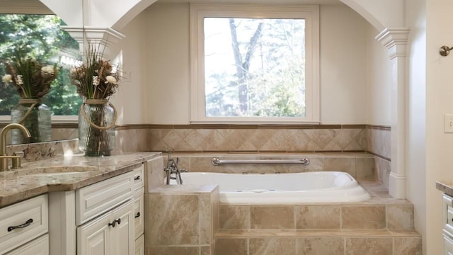 bathroom featuring a relaxing tiled tub, vanity, and ornate columns