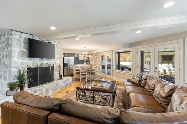 living room with crown molding, a notable chandelier, a stone fireplace, and french doors