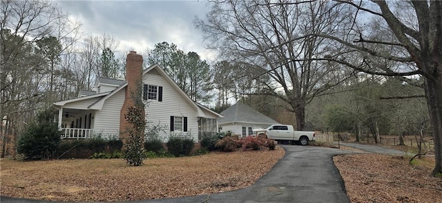 view of side of home with covered porch, driveway, and a chimney