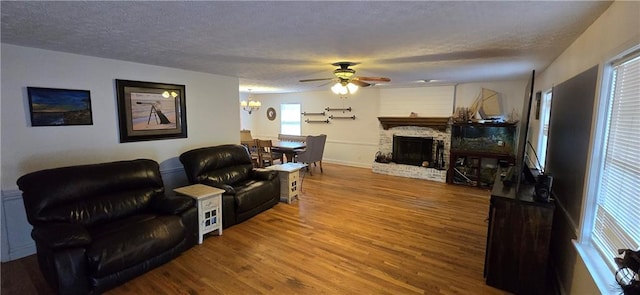 living room featuring a textured ceiling, ceiling fan with notable chandelier, a fireplace, and wood finished floors