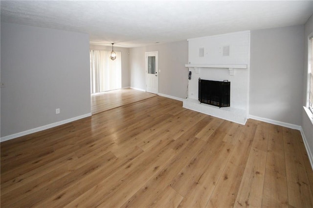 unfurnished living room with hardwood / wood-style floors, a notable chandelier, and a brick fireplace