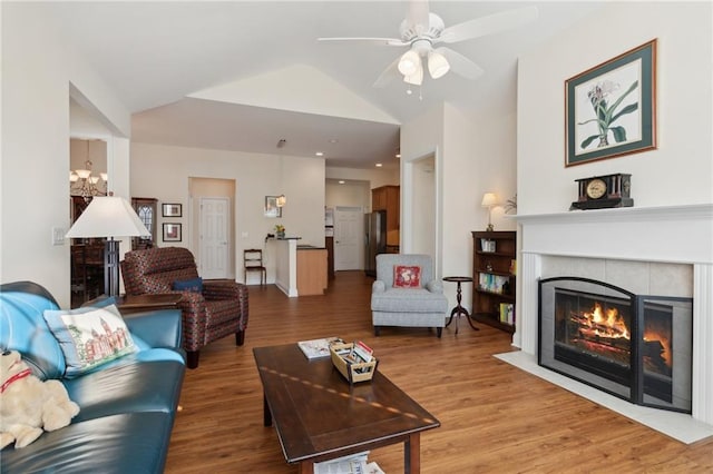 living room featuring wood-type flooring, ceiling fan with notable chandelier, lofted ceiling, and a tiled fireplace