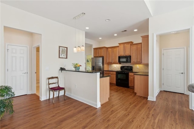 kitchen with pendant lighting, hardwood / wood-style floors, black appliances, tasteful backsplash, and kitchen peninsula