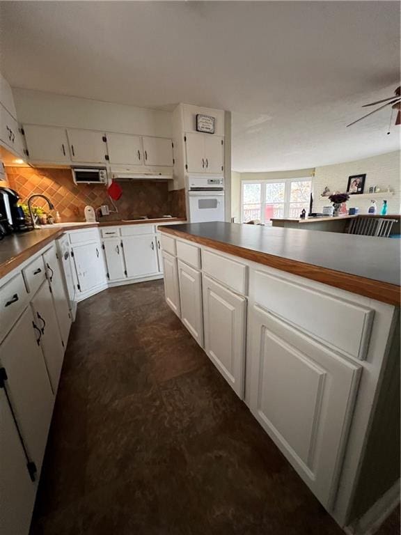 kitchen featuring decorative backsplash, white oven, ceiling fan, sink, and white cabinets