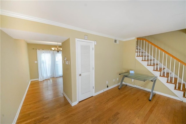 stairway featuring wood-type flooring, crown molding, and a notable chandelier