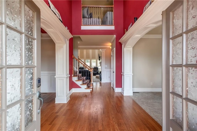 foyer entrance with a towering ceiling, hardwood / wood-style flooring, crown molding, and decorative columns