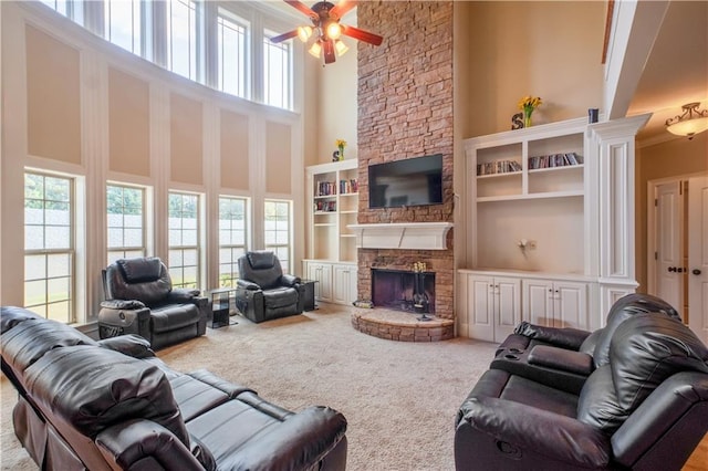 living room with ceiling fan, a stone fireplace, plenty of natural light, and a high ceiling