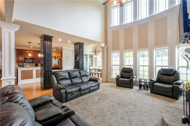 carpeted living room with ceiling fan, a towering ceiling, and decorative columns