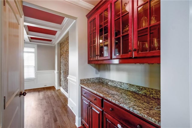 bar featuring coffered ceiling, light stone counters, beamed ceiling, wood-type flooring, and ornamental molding