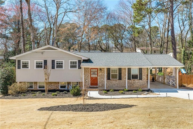 split level home with brick siding, fence, concrete driveway, a carport, and a front yard