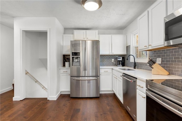 kitchen with light countertops, appliances with stainless steel finishes, dark wood-type flooring, white cabinetry, and a sink