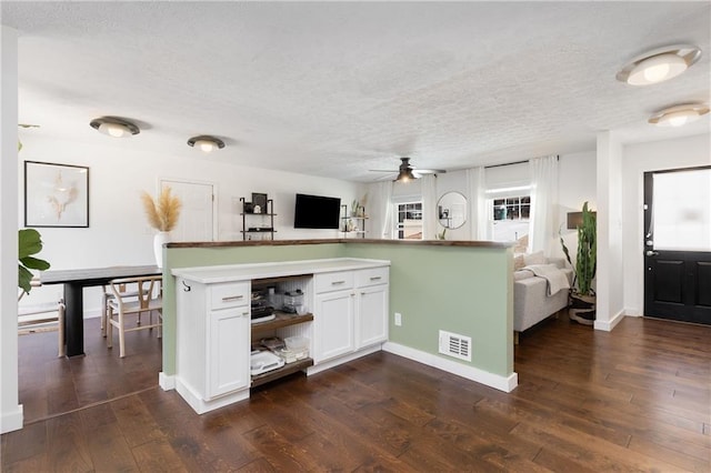 kitchen featuring a textured ceiling, dark wood-type flooring, visible vents, white cabinetry, and open floor plan