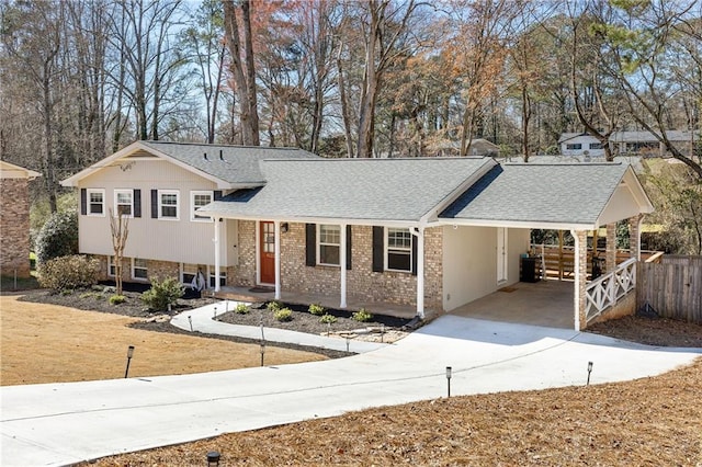 split level home with driveway, a shingled roof, an attached carport, fence, and brick siding