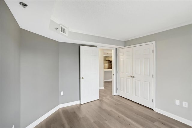 unfurnished bedroom featuring crown molding, light hardwood / wood-style floors, and a closet