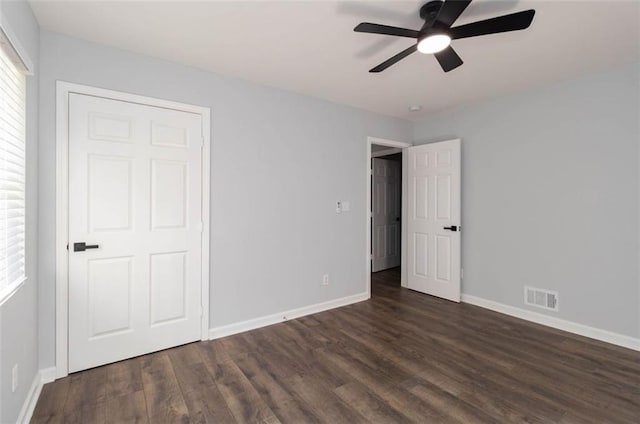 unfurnished bedroom with dark wood-type flooring, ceiling fan, a closet, and multiple windows