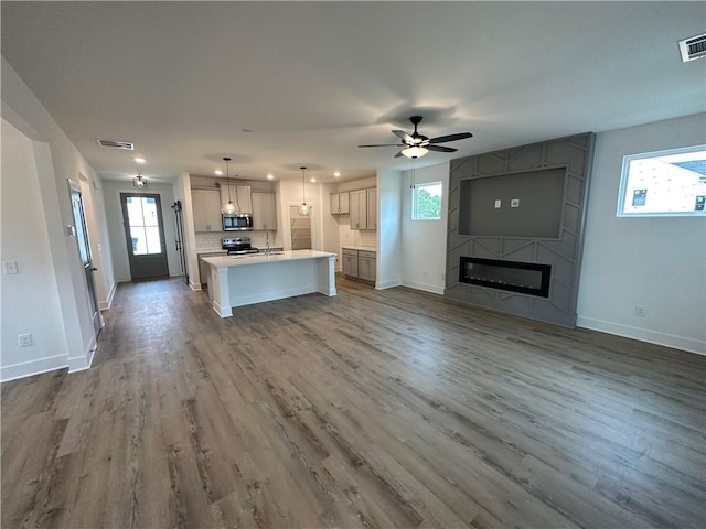 kitchen with appliances with stainless steel finishes, a fireplace, wood-type flooring, hanging light fixtures, and a center island with sink