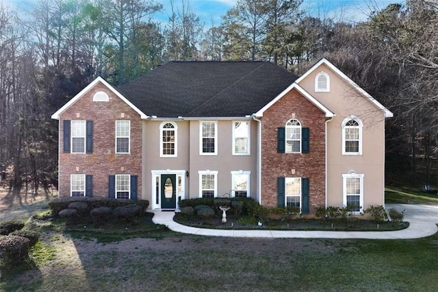 colonial house with a front lawn, stone siding, and stucco siding