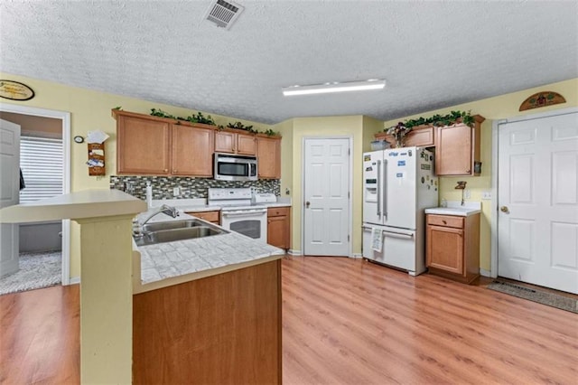 kitchen featuring visible vents, a sink, white appliances, brown cabinetry, and light countertops