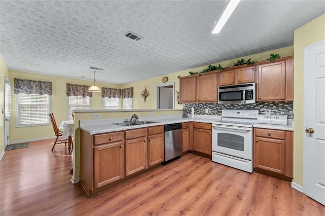 kitchen featuring visible vents, light wood-style flooring, stainless steel appliances, a peninsula, and brown cabinetry