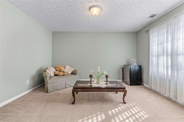 living area with carpet flooring, visible vents, a textured ceiling, and baseboards