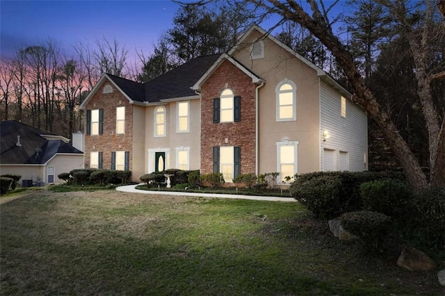 colonial inspired home featuring a yard, a garage, central AC unit, and stucco siding