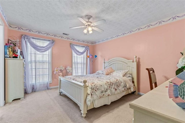 bedroom featuring light carpet, visible vents, a textured ceiling, and ceiling fan