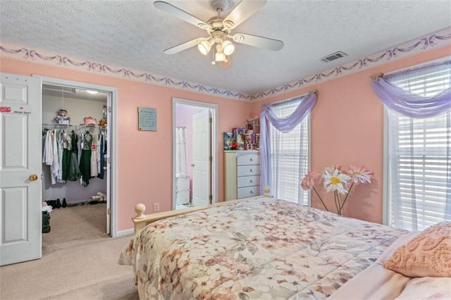 bedroom featuring a walk in closet, light carpet, a textured ceiling, and a closet