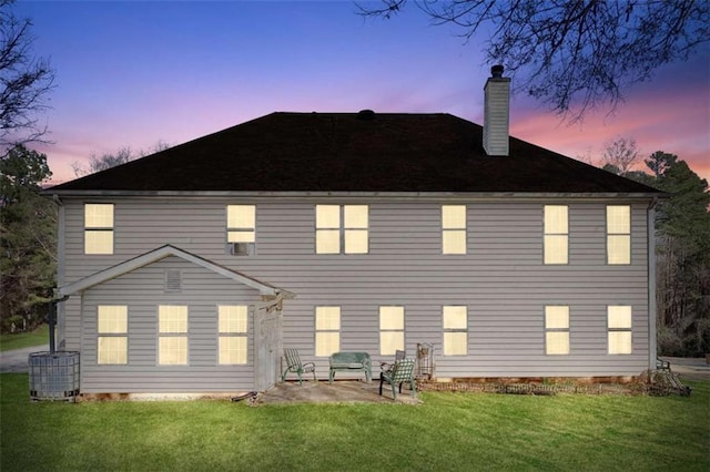 back of house at dusk with a lawn, a chimney, and a patio area