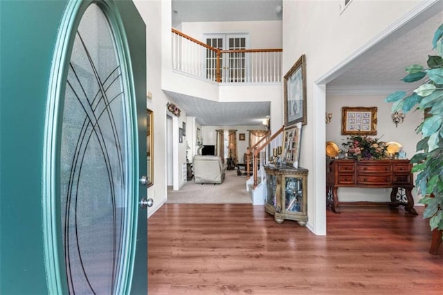 entryway featuring a high ceiling, wood finished floors, stairs, and crown molding