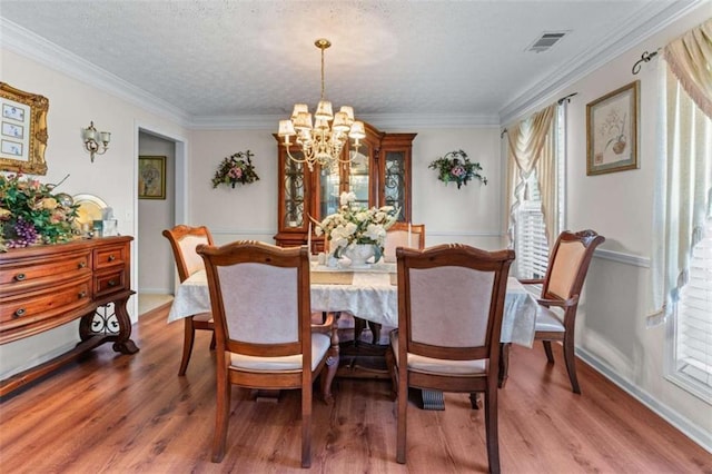 dining space featuring visible vents, a textured ceiling, wood finished floors, crown molding, and a chandelier